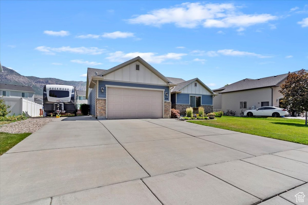 View of front facade featuring board and batten siding, concrete driveway, an attached garage, a front yard, and stone siding
