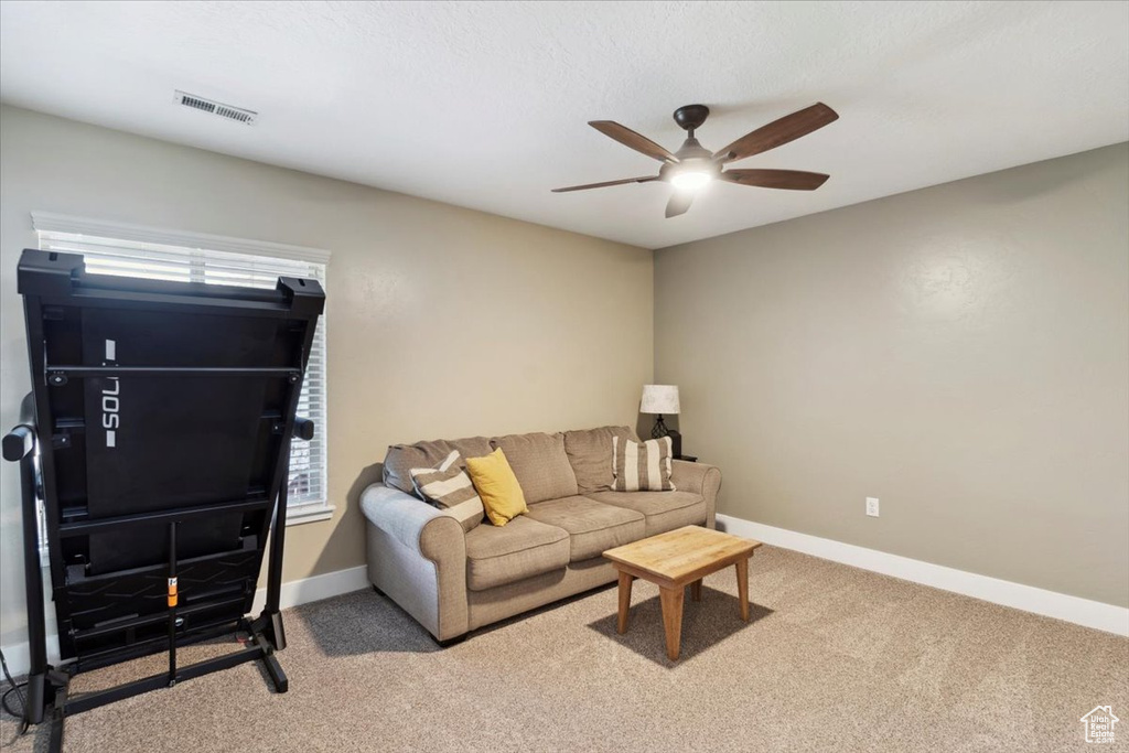 Carpeted living room featuring ceiling fan and baseboards