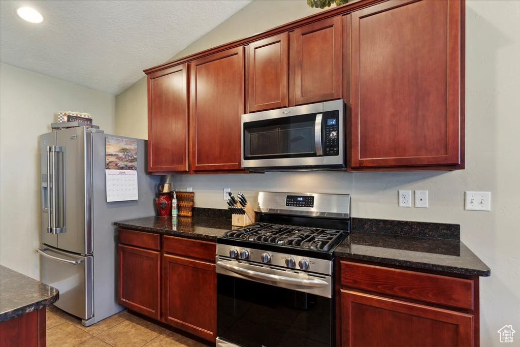 Kitchen featuring appliances with stainless steel finishes, lofted ceiling, dark brown cabinets, and light tile patterned floors