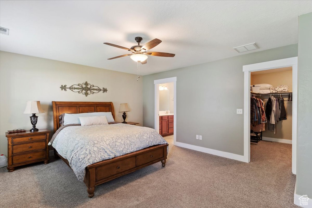 Bedroom with light carpet, a spacious closet, a closet, ensuite bath, and ceiling fan