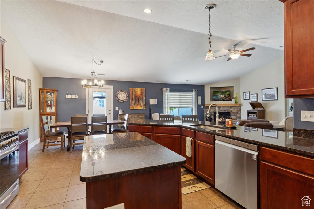 Kitchen with stainless steel appliances, a ceiling fan, a fireplace, hanging light fixtures, and lofted ceiling