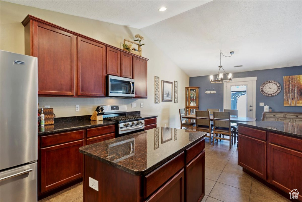 Kitchen with stainless steel appliances, lofted ceiling, reddish brown cabinets, dark stone counters, and a center island