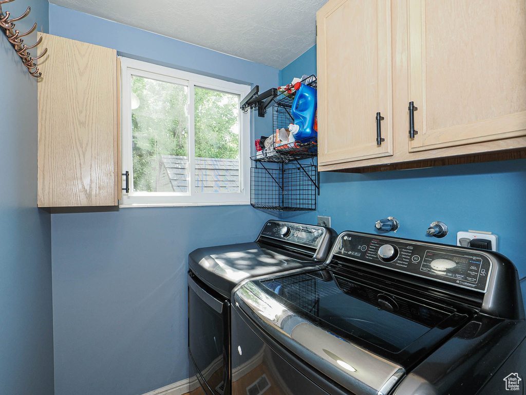 Washroom with washing machine and clothes dryer, cabinet space, and a textured ceiling