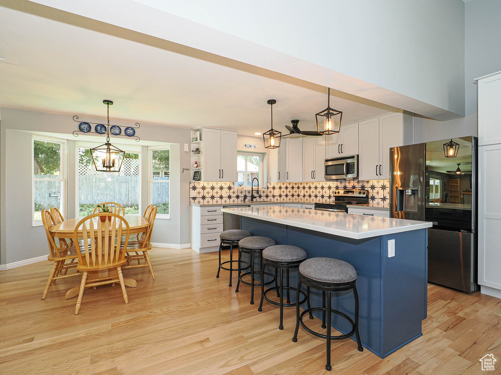 Kitchen featuring stainless steel appliances, a center island, light wood-style flooring, white cabinetry, and a breakfast bar area
