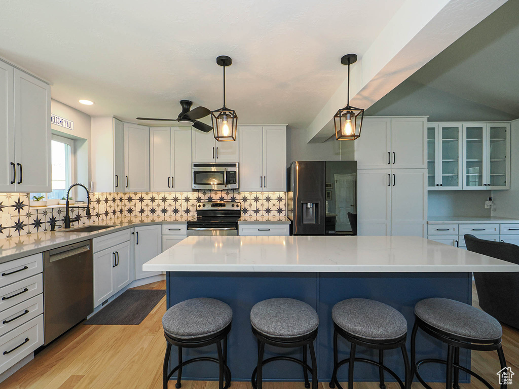 Kitchen with appliances with stainless steel finishes, white cabinetry, a kitchen bar, decorative backsplash, and recessed lighting