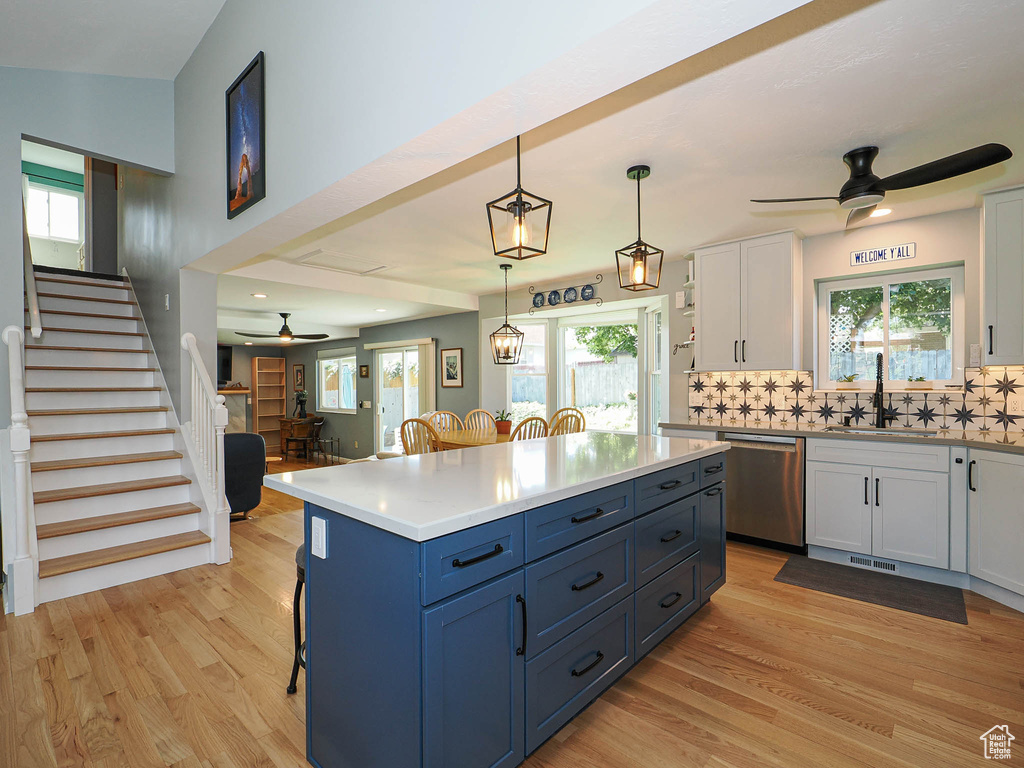 Kitchen with ceiling fan, stainless steel dishwasher, white cabinets, light wood-type flooring, and tasteful backsplash