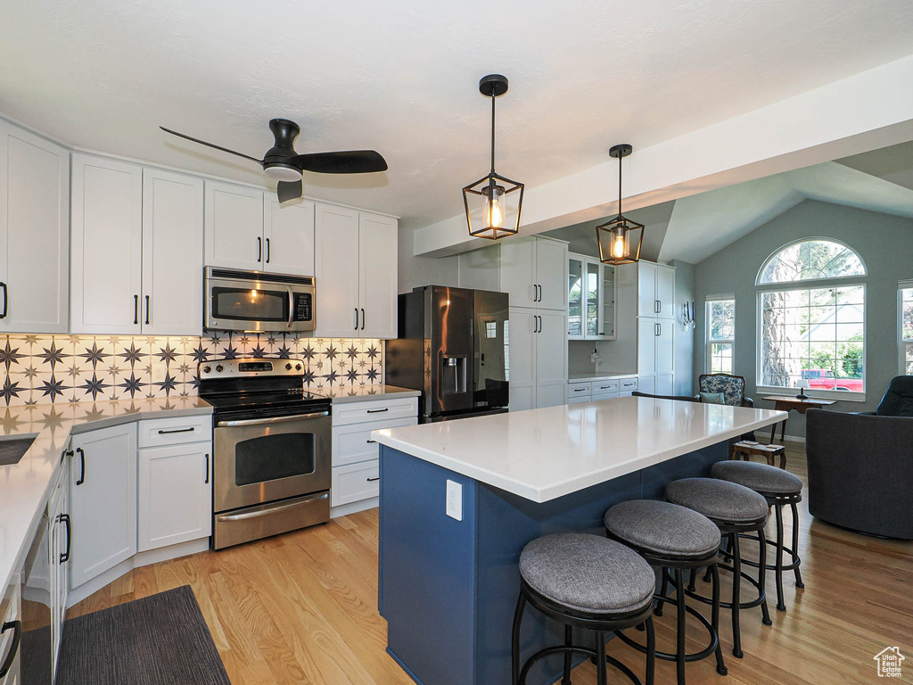 Kitchen featuring stainless steel appliances, a kitchen bar, light wood-type flooring, white cabinets, and lofted ceiling