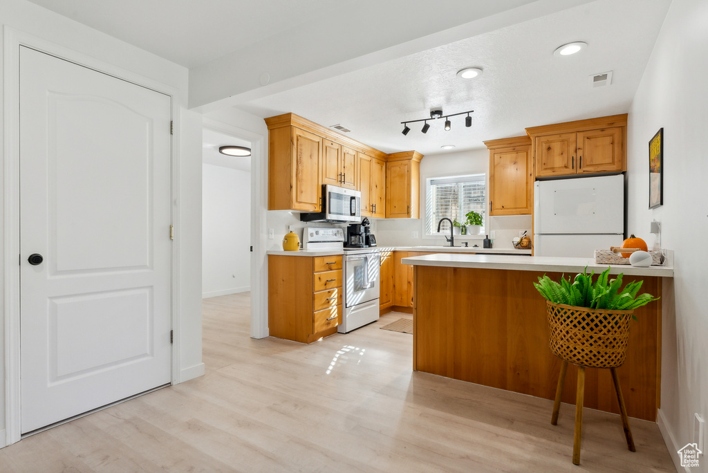Kitchen with white electric range oven, fridge, stainless steel microwave, light countertops, and light wood finished floors