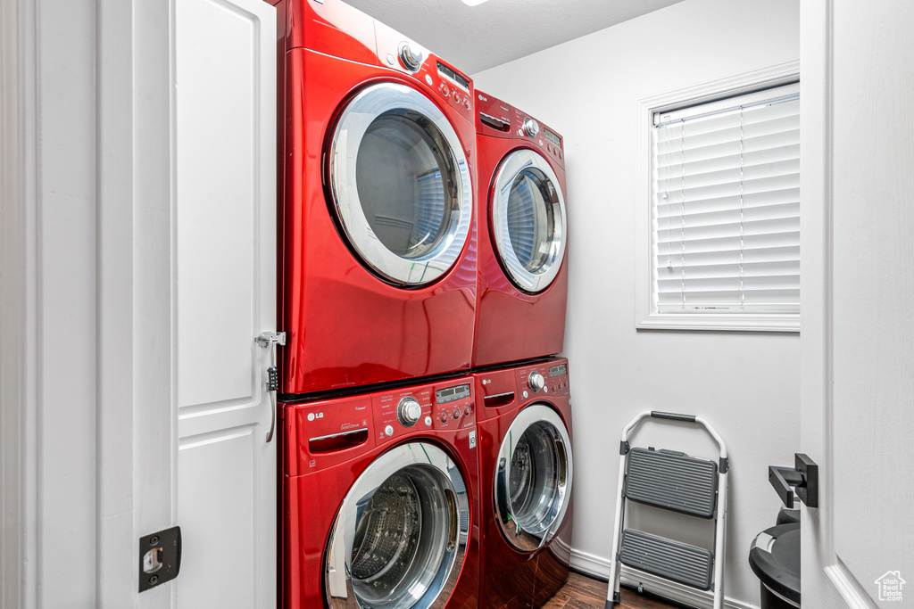 Laundry room with stacked washer and clothes dryer, wood finished floors, and heating unit