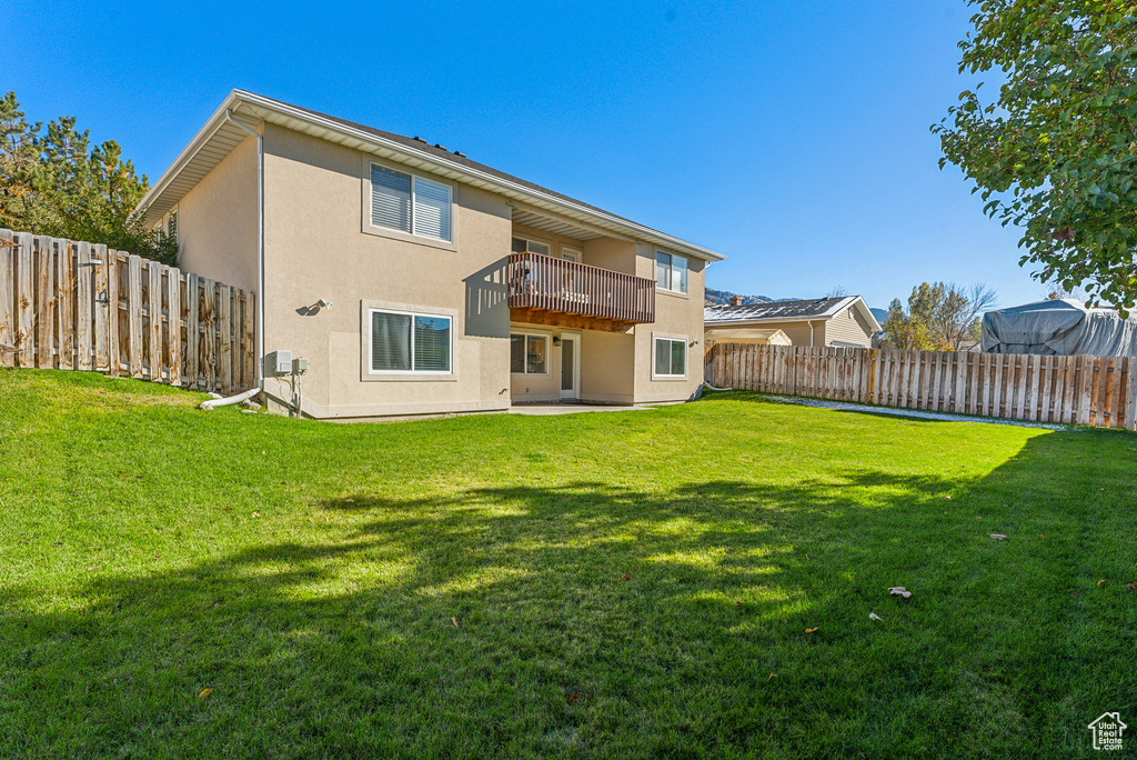 Rear view of house with stucco siding, a fenced backyard, and a balcony