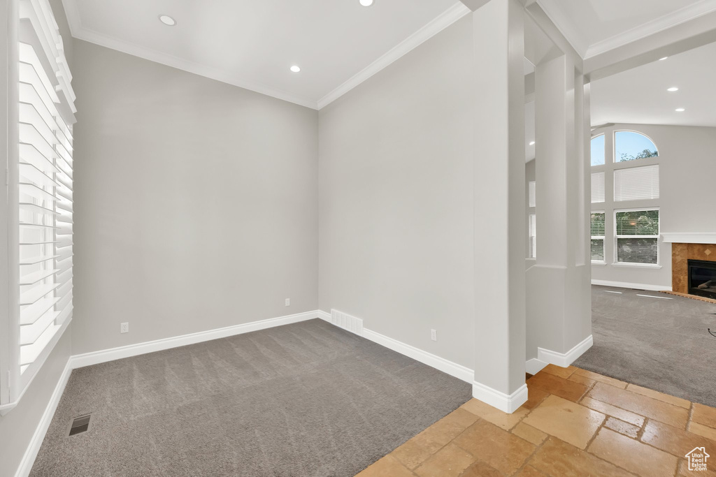 Empty room featuring carpet flooring, a tiled fireplace, stone tile floors, recessed lighting, and crown molding