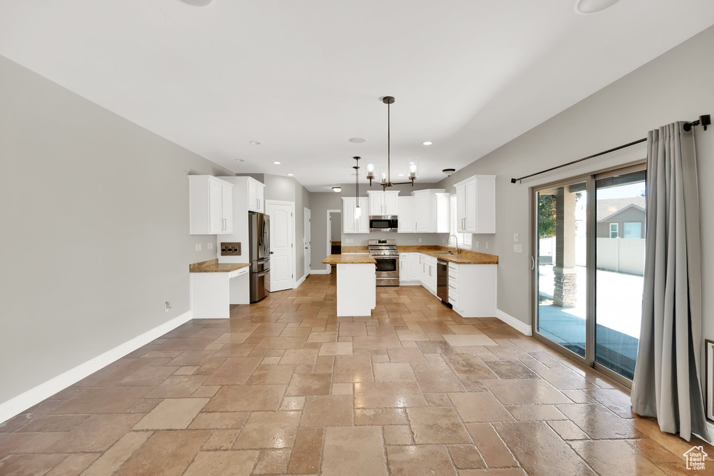 Kitchen with stainless steel appliances, stone tile flooring, recessed lighting, white cabinetry, and a kitchen island