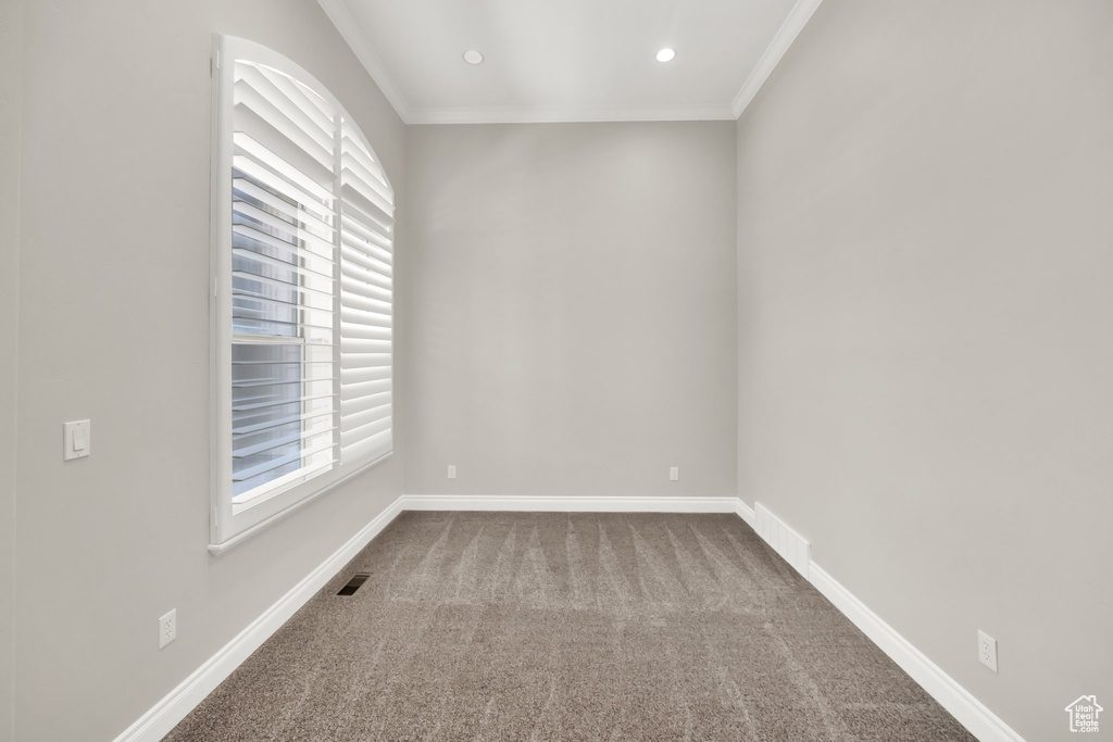 Spare room featuring dark carpet, plenty of natural light, crown molding, and recessed lighting