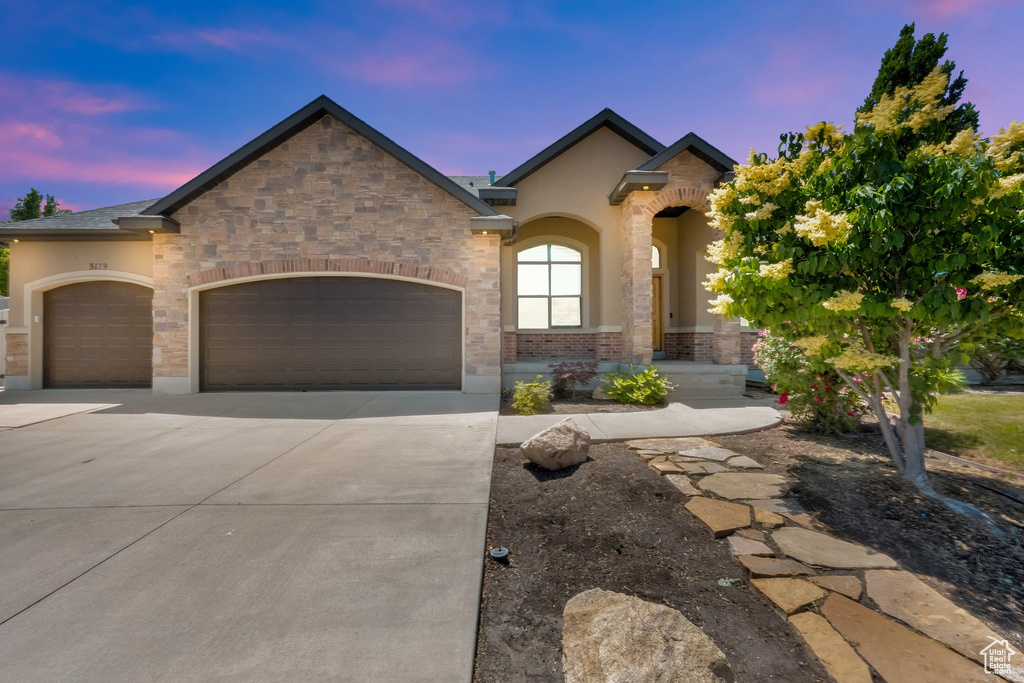 French provincial home with an attached garage, concrete driveway, and stucco siding