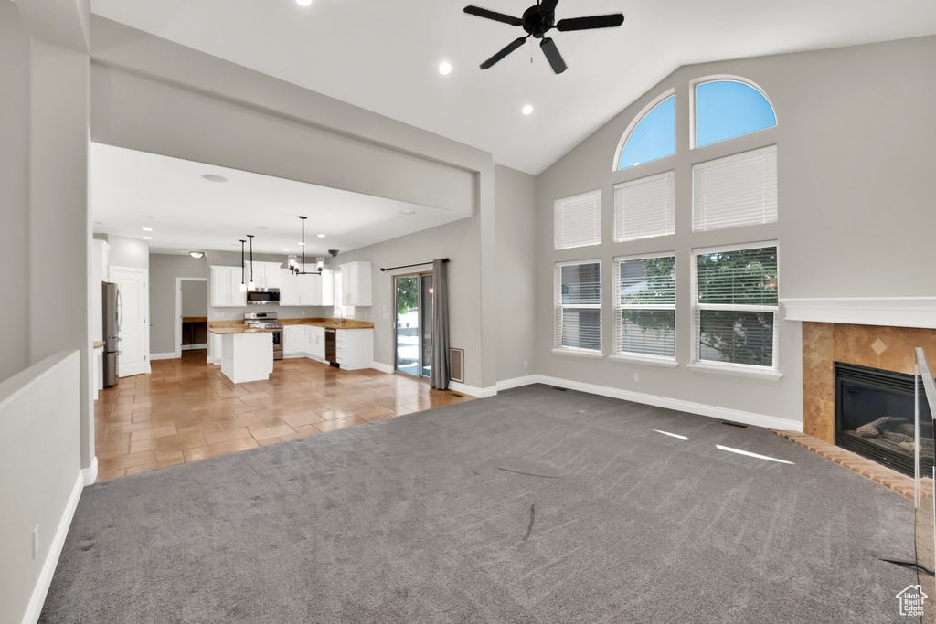 Unfurnished living room featuring ceiling fan, a tiled fireplace, recessed lighting, light colored carpet, and a chandelier