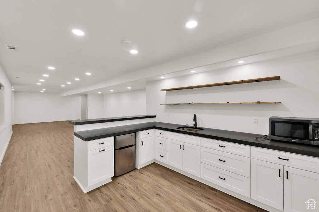 Kitchen featuring stainless steel fridge, open shelves, dark countertops, light wood-style flooring, and white cabinetry