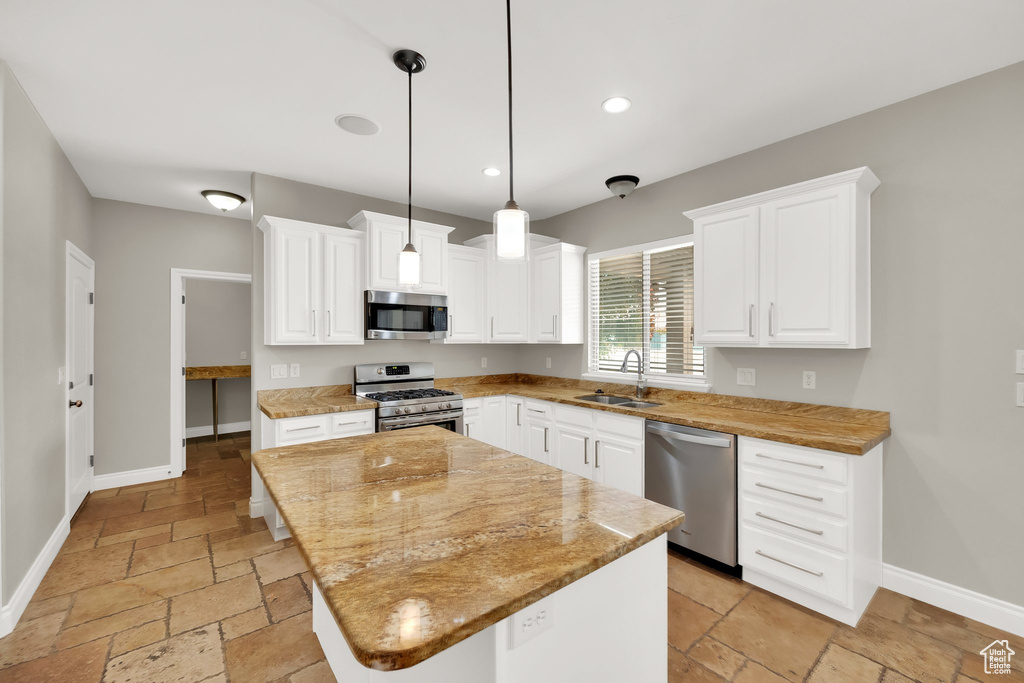 Kitchen with stainless steel appliances, stone tile floors, a center island, white cabinets, and recessed lighting