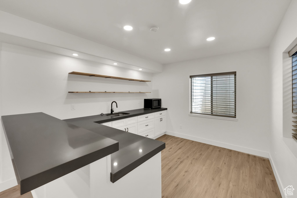 Kitchen featuring black microwave, dark countertops, open shelves, white cabinets, and light wood-style floors