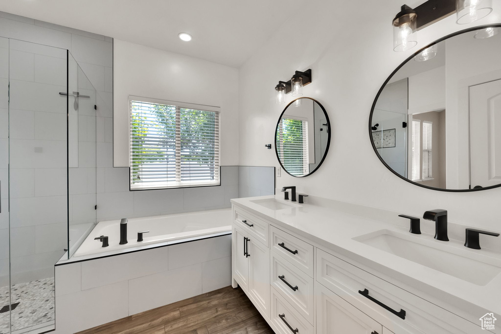 Bathroom with a bath, double vanity, wood finished floors, a shower stall, and recessed lighting