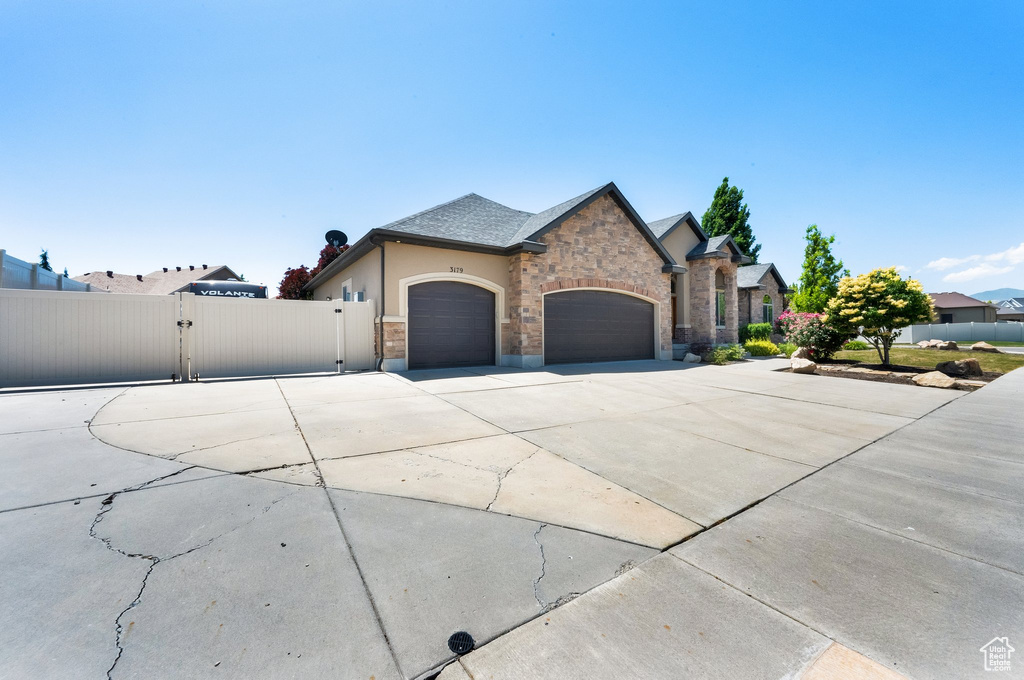 French country inspired facade with a gate, an attached garage, concrete driveway, stone siding, and stucco siding