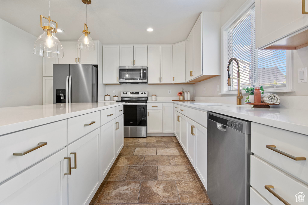 Kitchen with stainless steel appliances, stone finish flooring, white cabinets, recessed lighting, and light countertops