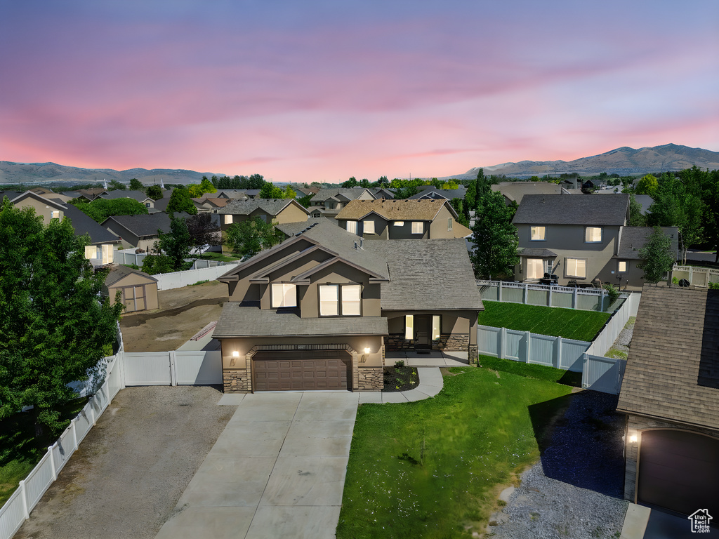 View of front of property with stone siding, a residential view, a mountain view, concrete driveway, and a fenced backyard