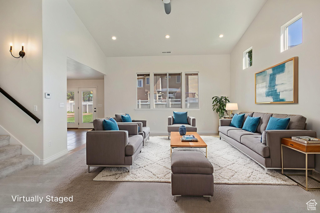 Carpeted living area with high vaulted ceiling, stairway, and recessed lighting