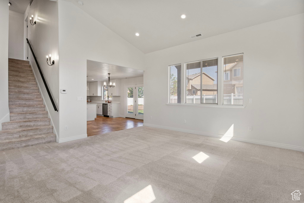 Unfurnished living room featuring carpet floors, recessed lighting, stairs, a chandelier, and high vaulted ceiling