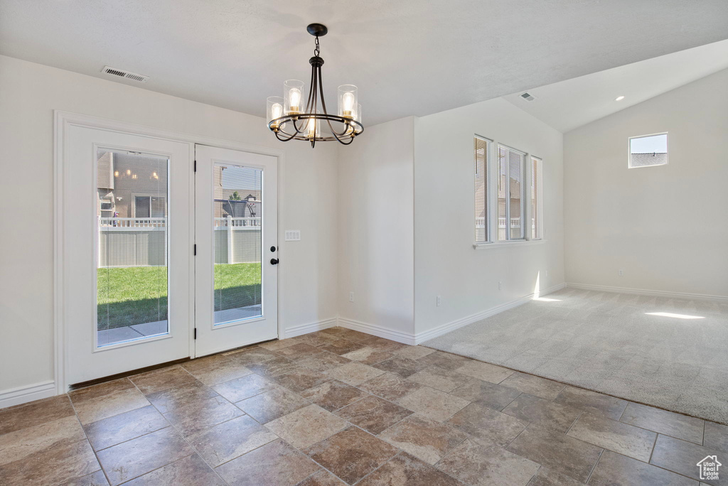 Doorway to outside with stone tile floors, a chandelier, and vaulted ceiling
