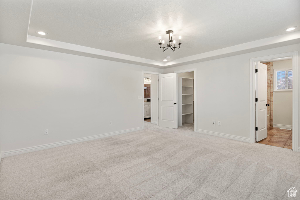 Unfurnished bedroom with a raised ceiling, a chandelier, a spacious closet, carpet flooring, and recessed lighting