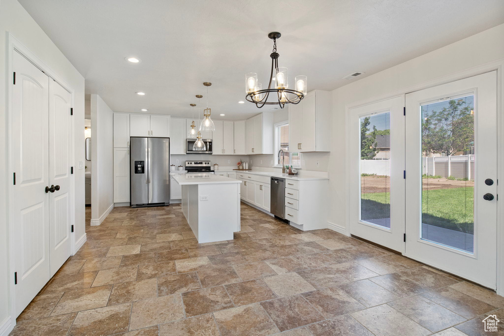 Kitchen featuring stainless steel appliances, stone tile flooring, light countertops, a chandelier, and white cabinetry