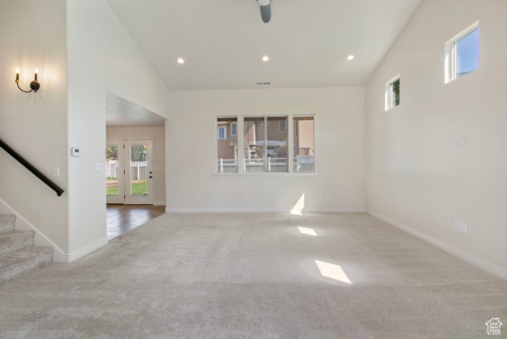 Carpeted empty room featuring healthy amount of natural light, high vaulted ceiling, stairs, recessed lighting, and ceiling fan