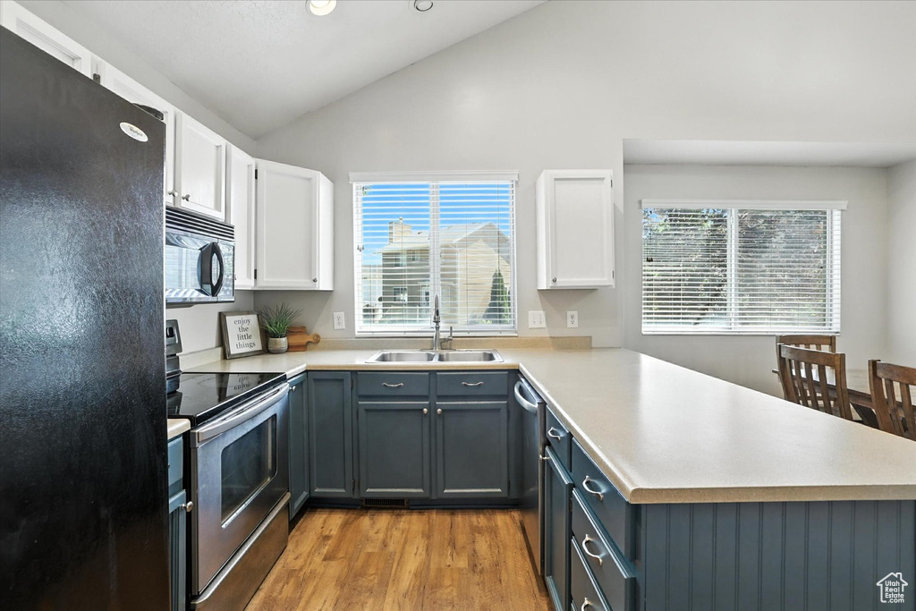 Kitchen with black appliances, a peninsula, light wood finished floors, white cabinetry, and light countertops