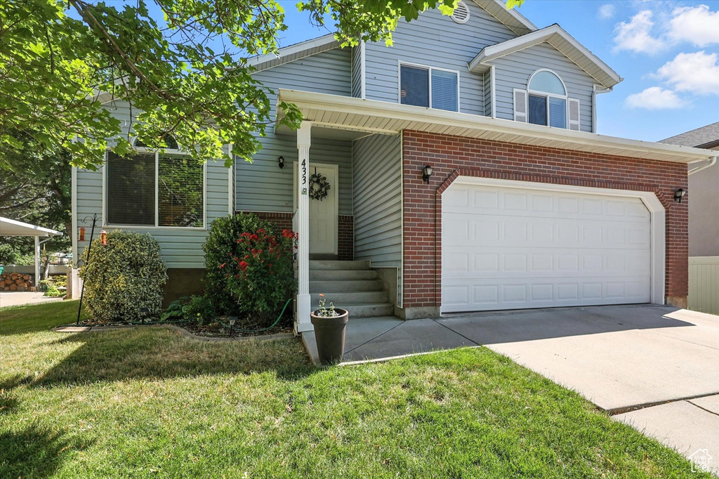 View of front of property featuring brick siding, concrete driveway, a front lawn, and a garage