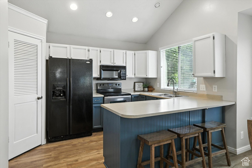 Kitchen with black appliances, a peninsula, white cabinetry, light countertops, and light wood-type flooring