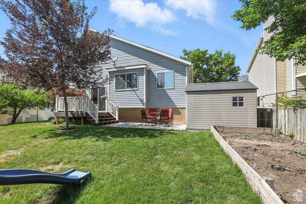 Back of house featuring a fenced backyard, a deck, a patio, and a garden