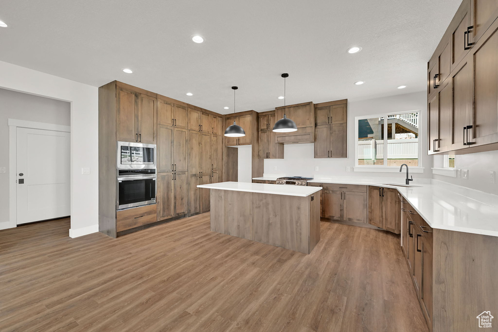 Kitchen featuring stainless steel appliances, light wood-style flooring, a center island, recessed lighting, and light countertops