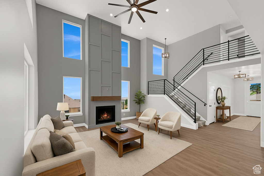 Living area featuring a high ceiling, light wood-style floors, stairs, a large fireplace, and a ceiling fan