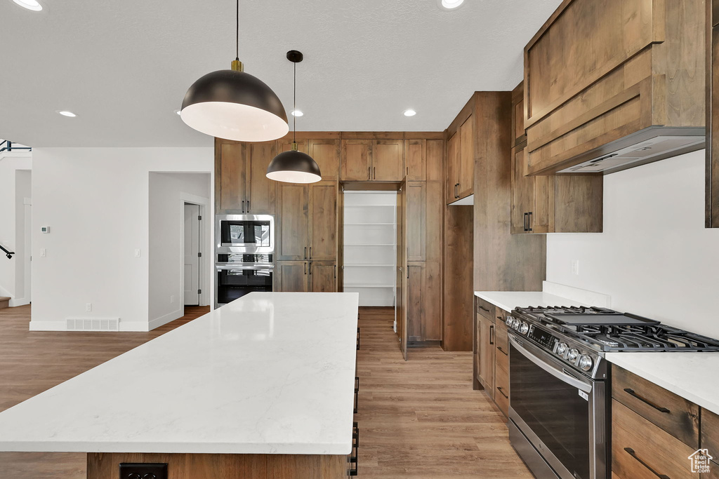 Kitchen with appliances with stainless steel finishes, light wood-style floors, recessed lighting, a center island, and hanging light fixtures