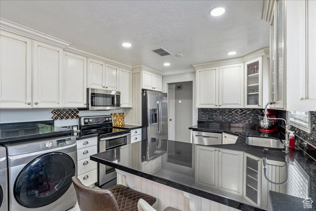Kitchen with stainless steel appliances, washing machine and dryer, a breakfast bar area, a peninsula, and glass insert cabinets