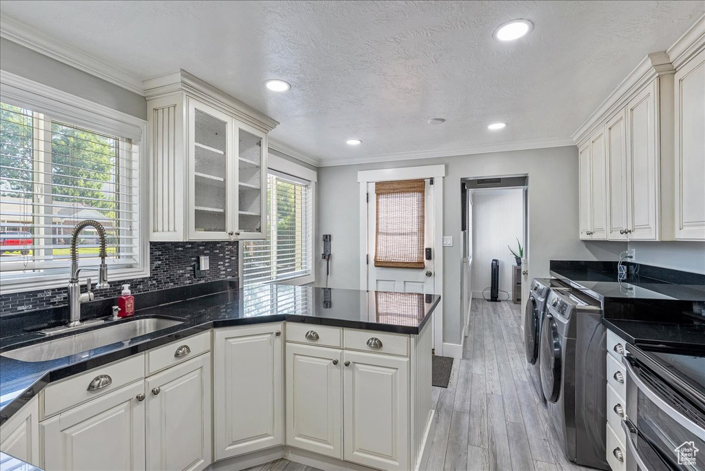 Kitchen featuring separate washer and dryer, a peninsula, light wood-type flooring, white cabinets, and ornamental molding