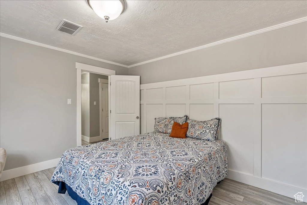 Bedroom with light wood finished floors, crown molding, and a textured ceiling