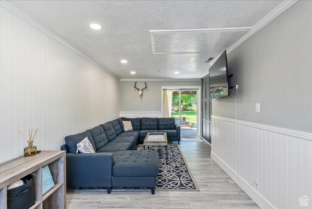 Living area featuring a textured ceiling, crown molding, a wainscoted wall, light wood-style flooring, and recessed lighting