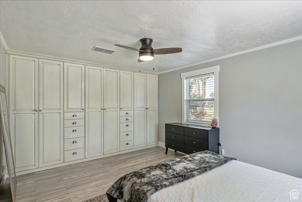 Bedroom with light wood finished floors, ornamental molding, a textured ceiling, and a ceiling fan