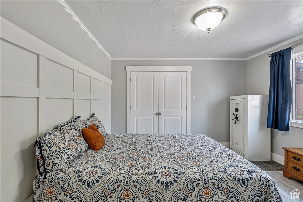 Bedroom with crown molding, wood finished floors, a textured ceiling, multiple windows, and a closet