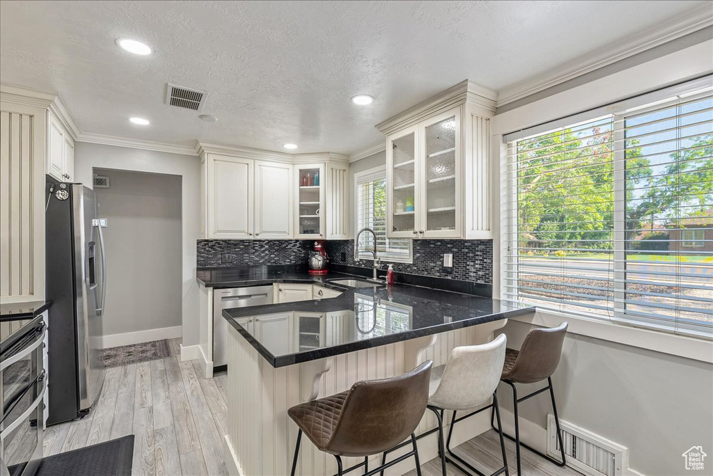 Kitchen with appliances with stainless steel finishes, a peninsula, decorative backsplash, a breakfast bar area, and glass insert cabinets