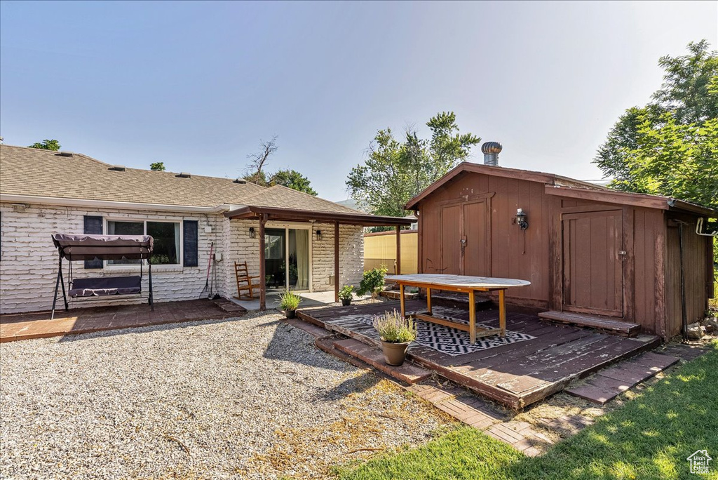 Back of property with a shed, a patio area, and a shingled roof