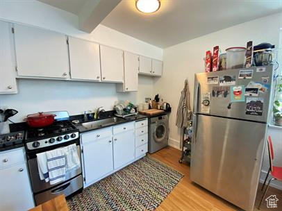 Kitchen featuring stainless steel appliances, washer / dryer, dark countertops, light wood-type flooring, and white cabinetry
