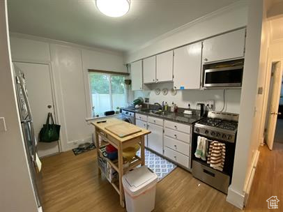Kitchen featuring stainless steel appliances, wood finished floors, dark countertops, ornamental molding, and white cabinetry
