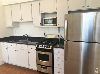 Kitchen featuring appliances with stainless steel finishes, wood finished floors, dark countertops, and white cabinets